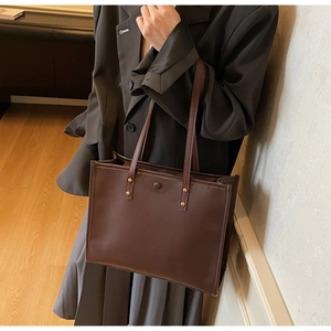 Detail of a large brown vintage tote bag with gold rivets worn on shoulder for commute