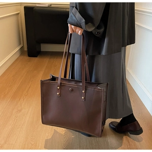 Detail view of large dark brown leather tote bag with gold rivets and magnetic closure