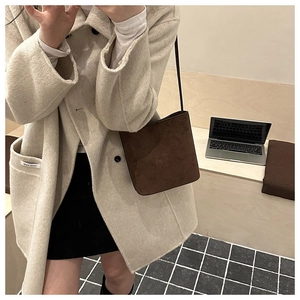 Detail of dark brown suede bucket bag worn cross-body with a minimalist shoulder strap