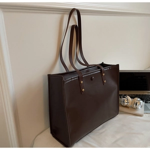 Close-up of a large brown vintage tote bag with gold metal rivet details on the straps