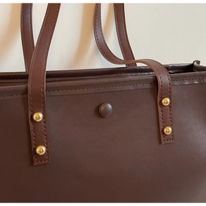 Detail of brown leather tote bag showing gold rivets and a snap closure for secure storage