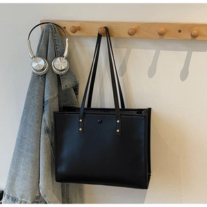 Detail view of large black retro tote bag with gold rivets hanging on a wooden wall hook