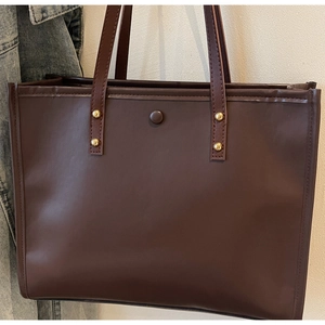 Macro detail of dark brown leather tote bag showing golden rivet hardware and magnetic clasp