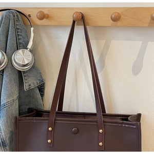 Detail of dark brown tote bag with gold rivets hanging on a wooden wall hook