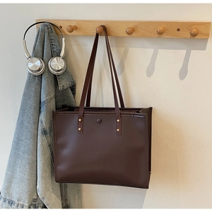 Detail of vintage brown leather tote bag with sturdy straps and rivet hardware on a hook