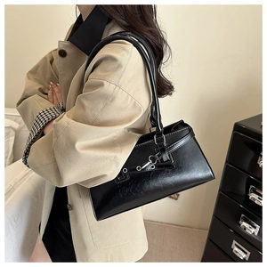 Detail of a black leather-textured trapezoid handbag with dual straps and metal hardware