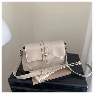 Close-up of beige crossbody bag with gold metal buckle on a dark mirrored surface