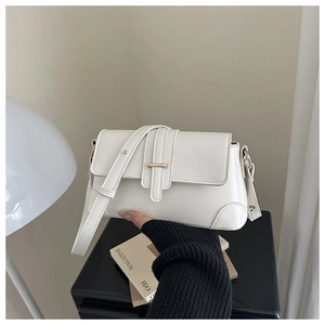 Detailed shot of cream white leather bag with gold hardware held in a stylish indoor setting
