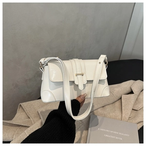 Detail of a creamy white PU leather shoulder bag with a gold buckle in a minimalist setting