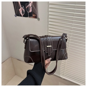 Detail of dark brown leather shoulder bag with white contrast stitching and gold buckle