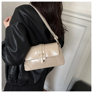 Close-up of a cream patent leather shoulder bag with vintage buckle and retro piping detail