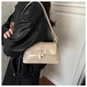 Detail of a beige glossy leather shoulder bag with gold metal buckle and flap closure