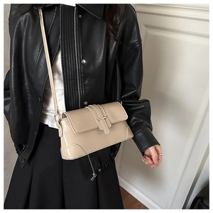 Detail of a cream crossbody bag with gold buckle on a model in a black leather jacket