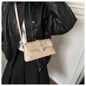 Close-up of beige crossbody bag with gold buckle on a model in a black leather jacket