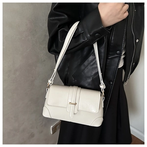 Detail of cream rectangular handbag with gold buckle and adjustable strap on model