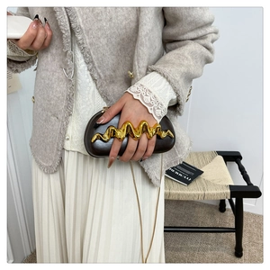 Detail einer eleganten dunkelbraunen Clutch mit goldenem Wellengriff und feiner Metallkette