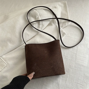 Minimalist dark brown suede bucket bag with slim shoulder strap on a striped background
