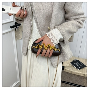 Detail of elegant brown leather clutch with unique golden wave metal handle and chain strap