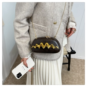 Detail of dark brown capsule crossbody bag with gold wave handle and chain strap