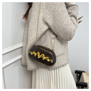 Detail of dark brown leather crossbody bag with wave gold metal decor on a model