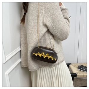 Detail der dunkelbraunen ovalen Abendtasche mit goldenem Wellendekor am Tweed-Outfit