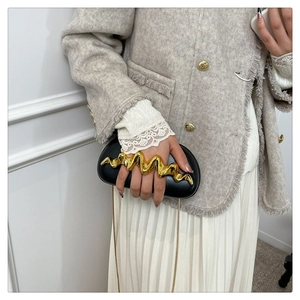 Detail of a black evening clutch bag with liquid wave metal handle and gold chain strap