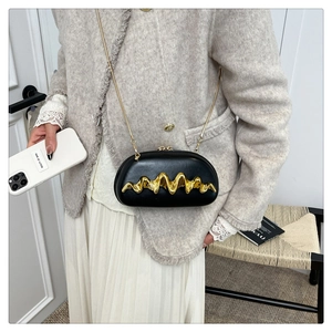 Detail of black oval evening clutch with gold wavy metal decoration and fine chain strap