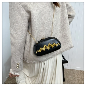 Detail of black wave pattern evening bag with gold metal trim and chain strap on a model