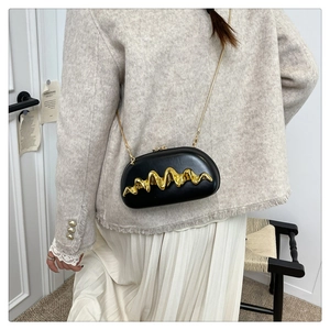 Detailansicht einer schwarzen Leder-Box-Tasche mit goldenem Wellenmuster-Metall
