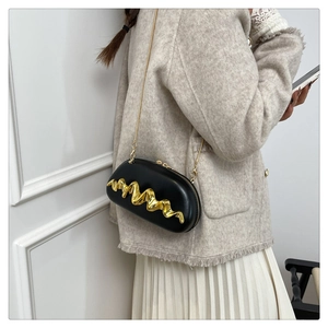 Detail view of a black hard-shell clutch with elegant golden wave metal pattern and chain