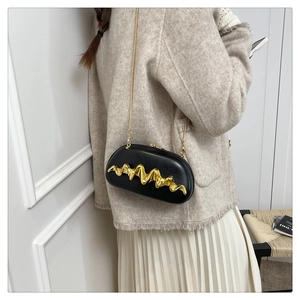 Detail view of wave pattern gold metal decoration on a black evening capsule bag