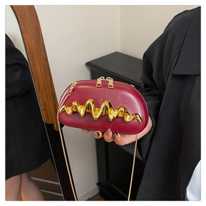 Detail der weinroten halbkreisförmigen Clutch mit Wellen-Metallverzierung und Goldkette