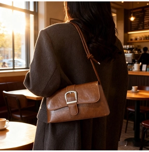 Close-up of brown vintage leather baguette bag with silver metal buckle on a shoulder strap