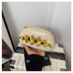 Detail der goldenen Wellen-Metallverzierung auf der cremefarbenen Kapsel-Clutch