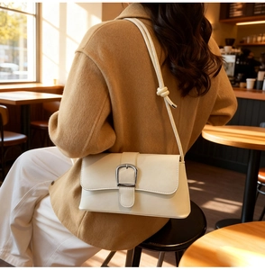 Close-up of cream leather shoulder bag featuring a decorative silver horseshoe buckle and knot detail