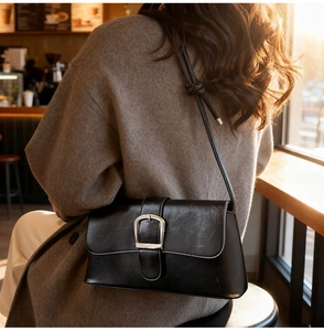 Close-up of black polished faux leather shoulder bag with a silver buckle in a cafe