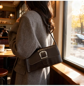 Detail of a dark brown patent leather baguette bag with a large silver metal buckle