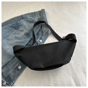 Detail of black PU leather crescent crossbody bag with adjustable nylon strap on denim