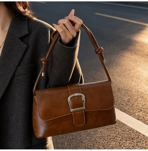 Detailed view of brown leather bag with silver metal buckle and shoulder strap knot