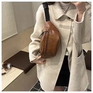 Close-up of brown PU leather crossbody chest bag with adjustable strap on a beige coat