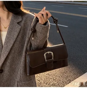 Detail of dark brown baguette bag with silver buckle and knotted shoulder strap