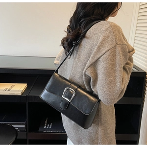 Detail of black leather shoulder bag featuring a silver metal buckle and knotted strap