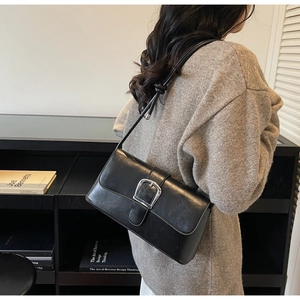 Detail view of black oil-wax leather baguette bag with silver buckle and knotted strap
