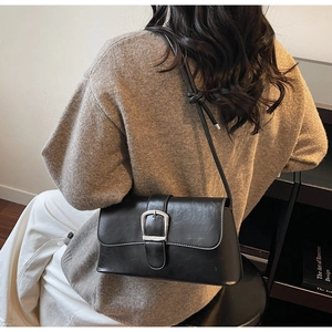 Detail of a vintage black leather baguette bag with a silver buckle worn by a model