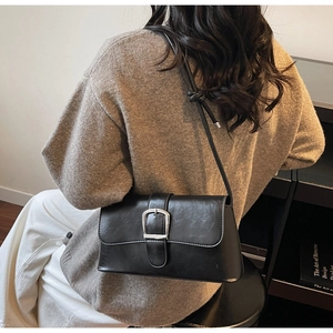 Detail of a vintage black patent leather shoulder bag with silver buckle on a model