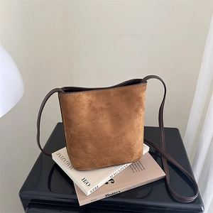Chic brown suede bucket bag with leather strap on magazines, minimalist autumn fashion style