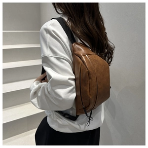 Brown leather saddle bag detail showing texture and adjustable black wide shoulder strap