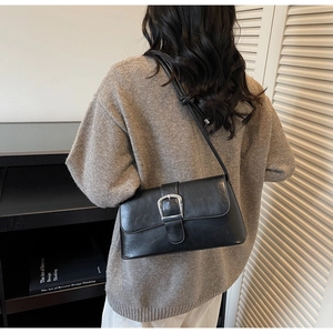 Side view of black faux leather baguette bag with silver buckle worn by a model