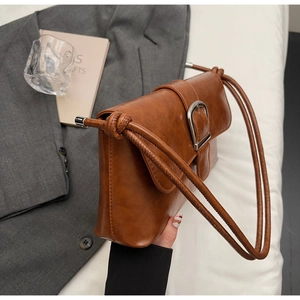 Detail of tan faux leather shoulder bag featuring a metal buckle and knot strap detail