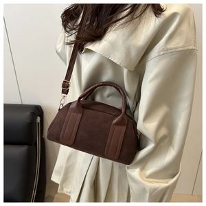 Dettaglio di una borsa Boston in camoscio marrone con finiture dorate su un trench neutro